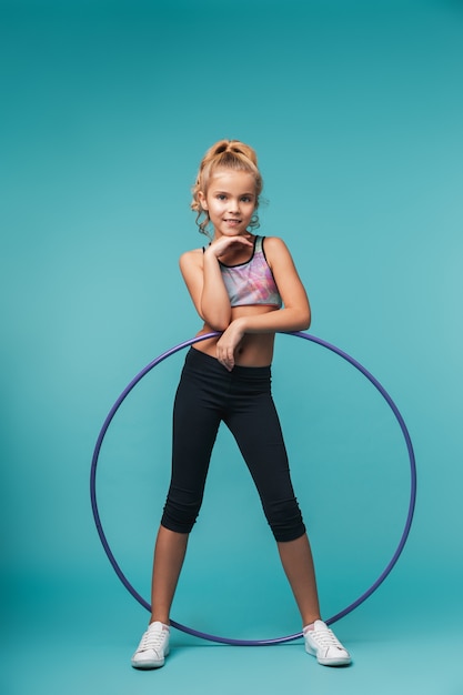 Фото Веселая маленькая спортивная девочка делает упражнения с обручем на синей стене