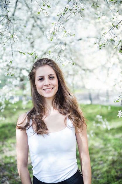 Cheerful long hair young woman in a white t-shirt under the blooming trees.