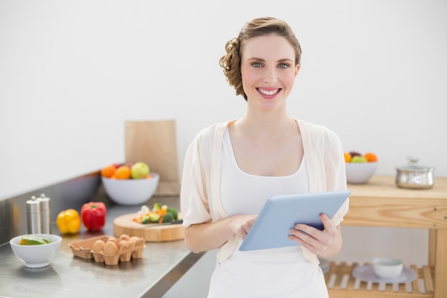 Cheerful lovely woman holding her tablet standing in her kitchen