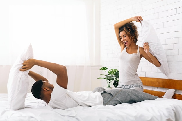 Cheerful loving couple is fighting by pillows in bed