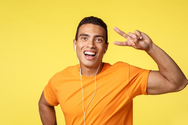 Cheerful, lucky smiling man in orange t-shirt, listen motivational music in earphones