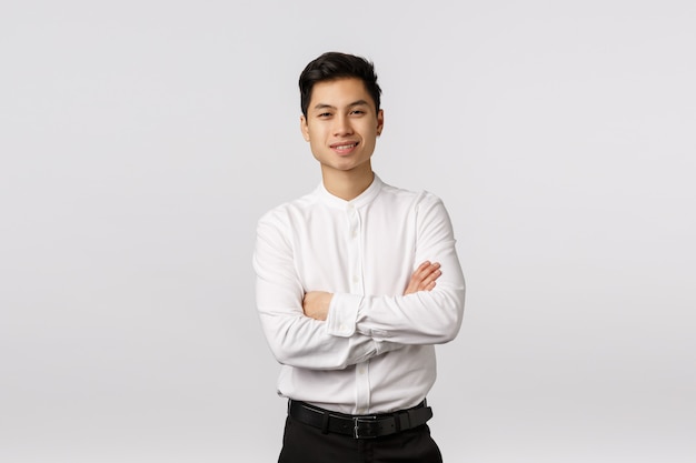 Веселый, удачливый и успешный симпатичный азиатский молодой предприниматель, закончивший бизнес-школу и готовый справиться с любой задачей, скрестив руки на груди, довольный улыбкой