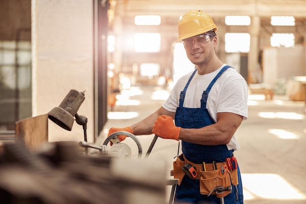 Веселый строитель-мужчина, использующий профессиональное оборудование в мастерской
