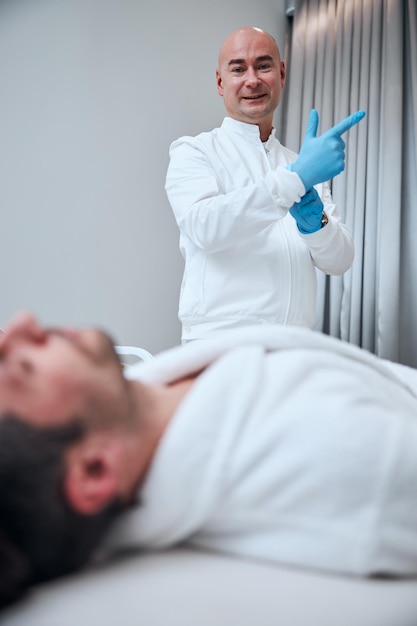 Cheerful male doctor examining handsome guy in office