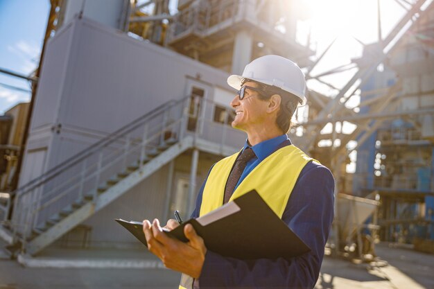 Cheerful male engineer doing paperwork outdoors at factory