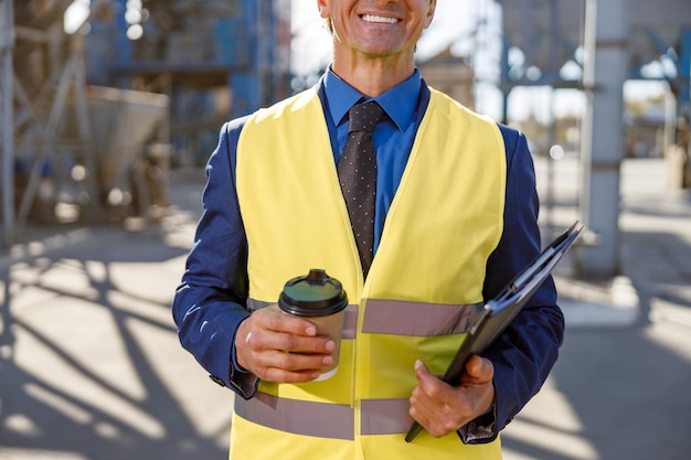 Cheerful male engineer holding cup of coffee and documents