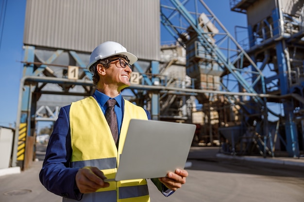 Cheerful male engineer using notebook outdoors at factory