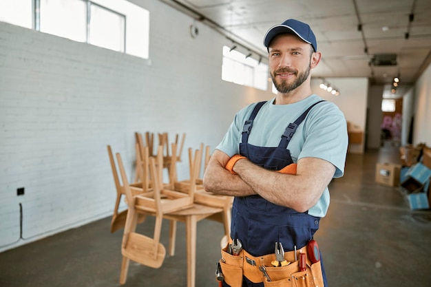 Cheerful male worker in cap standing in workshop