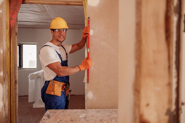 Веселый рабочий-мужчина измеряет стену в доме