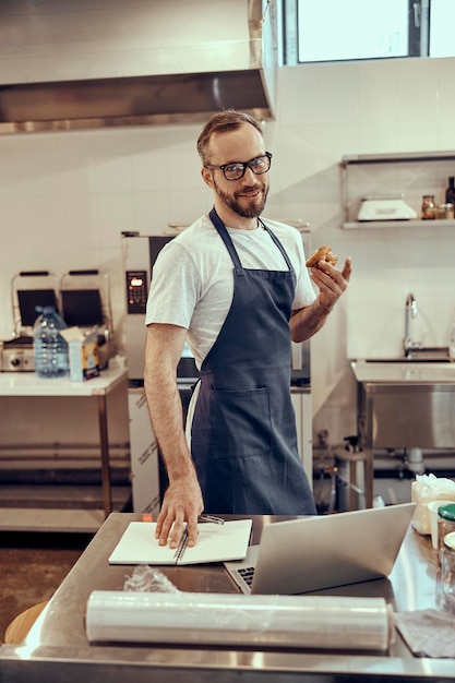 Cheerful male worker standing by the table with laptop in cafe