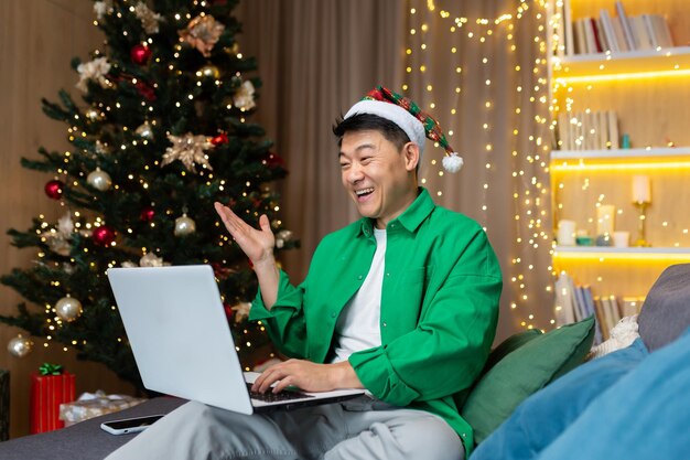 Cheerful man in christmas hat and green shirt talking with friends on video call asian man