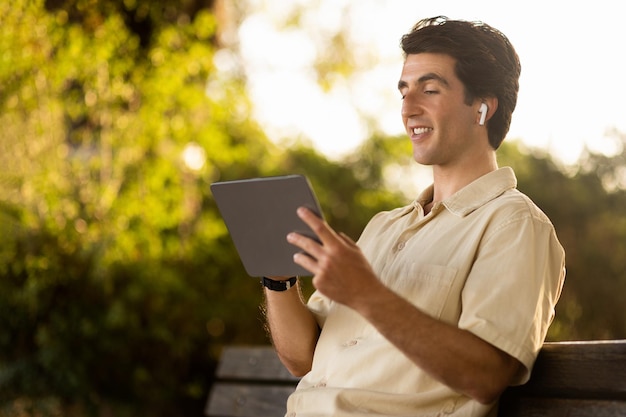 Cheerful man enjoying nice podcast resting on bench at park