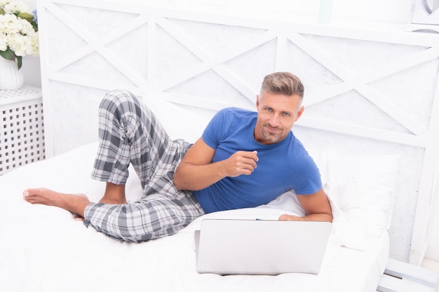 노트북으로 집에 있는 남자 프리랜서의 침실 사진에 있는 쾌활한 남자 프리랜서