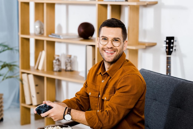 Веселый мужчина в очках с геймпадом в гостиной