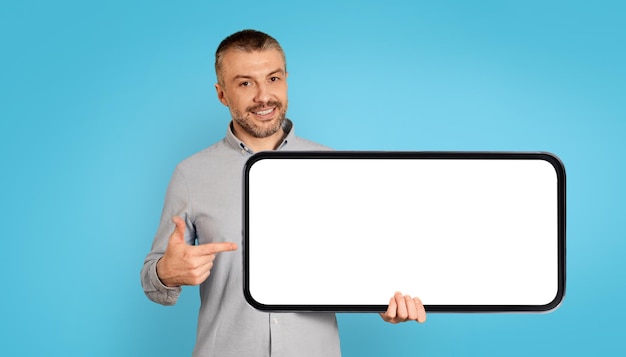 Cheerful Man Holding Large Smartphone With Empty Screen Blue Background