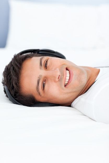 Photo cheerful man listening music with headphones lying on his bed