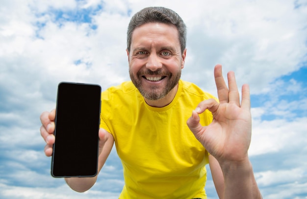 Cheerful man presenting screen of smartphone with copy space