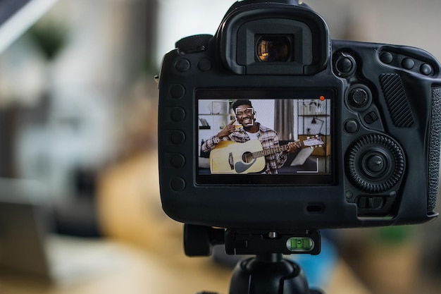 Cheerful man recording video on camera while playing guitar