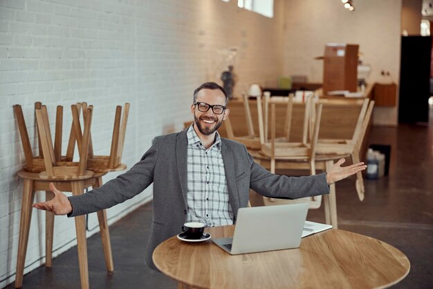 Веселый мужчина сидит за столом и пользуется ноутбуком в кафе