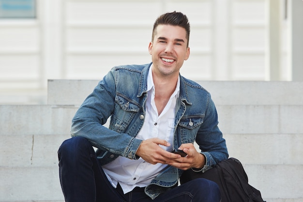 Cheerful man smiling and sitting with cellphone outside