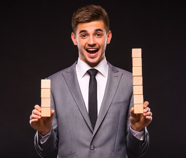 Cheerful man stands in a suit and holds wooden cubes.