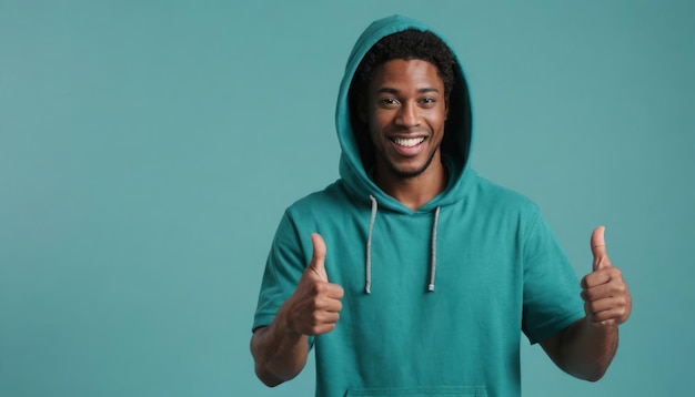 A cheerful man in a teal hoodie gives two thumbs up showcasing a relaxed and happy demeanor against