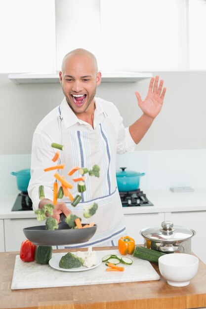 Cheerful man tossing vegetables in kitchen