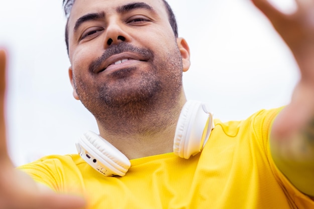 A cheerful man wearing a vibrant tshirt and wireless headphones playfully poses with a taking selfie