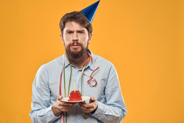 Cheerful man with a cake on a yellow background birthday holidays cap on his head person