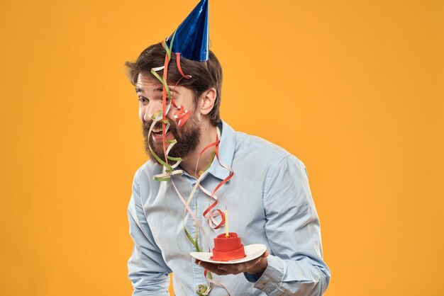 Cheerful man with a cake on a yellow background birthday holidays cap on his head person