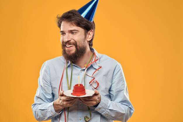 Cheerful man with a cake on a yellow background birthday holidays cap on his head person