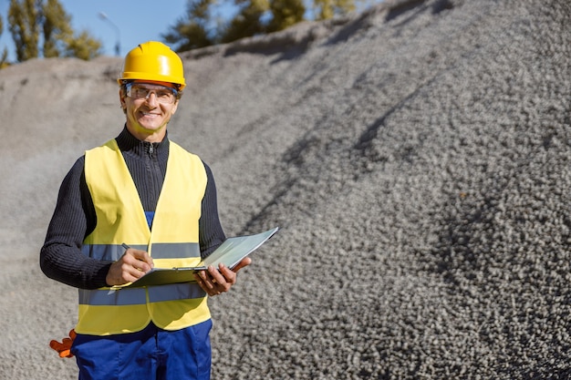 Cheerful man with documents standing outdoors at cement factory