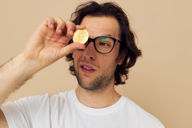 Cheerful man with glasses gold bitcoin in hands beige background. High quality photo