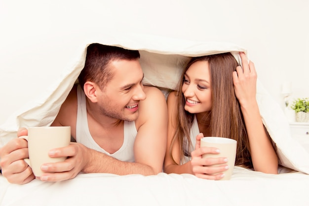 Cheerful man and woman basking with blanket and hot tea