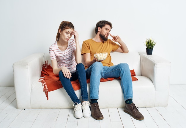 Cheerful man and woman on the couch with popcorn and red plaid flower in a pot emotions