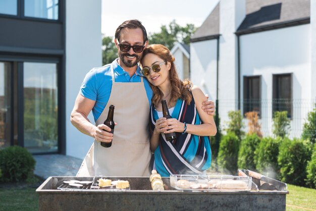 Cheerful married couple grilling meat while drinking bear together