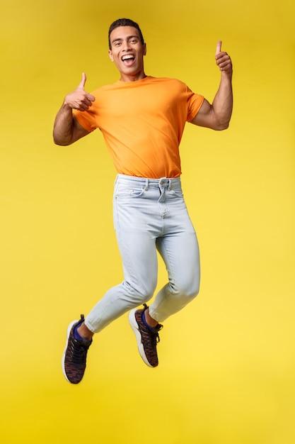 Cheerful masculine hipster guy in trendy orange t-shirt, jumping from happiness and joy