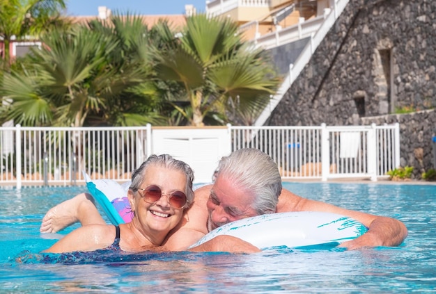 Cheerful mature adult active happy senior couple of grandparents relaxing in the swimming pool