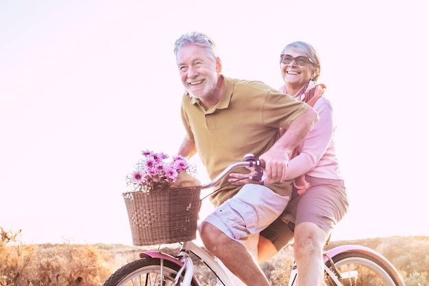 Cheerful mature couple of senior enjoy the outdoor leisure activity together riding a bike and laughing a lot