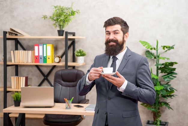 Cheerful mature entrepreneur in jacket having coffee break at office business