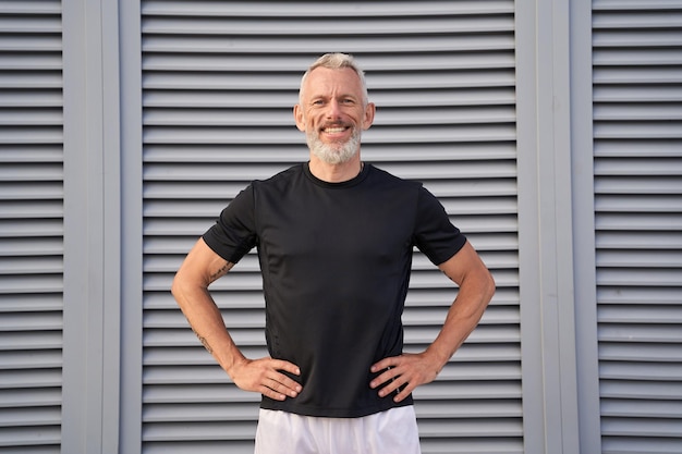 Cheerful mature man smiling at camera while standing posing outdoors over gray background