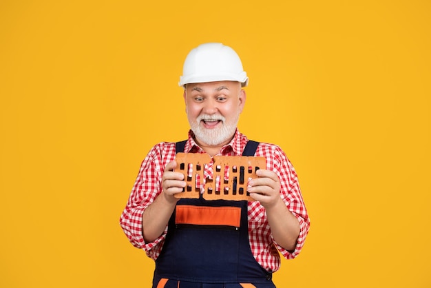 Cheerful mature man worker in helmet on yellow background