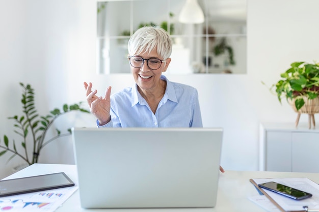 Cheerful mature woman having a video call from home, Online business concept. Senior woman explaining with her hands. business, businesswoman having video conference by laptop computer at office