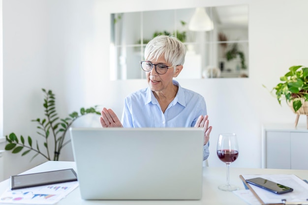 Cheerful mature woman having a video call from home, Online business concept. Senior woman explaining with her hands. business, businesswoman having video conference by laptop computer at office