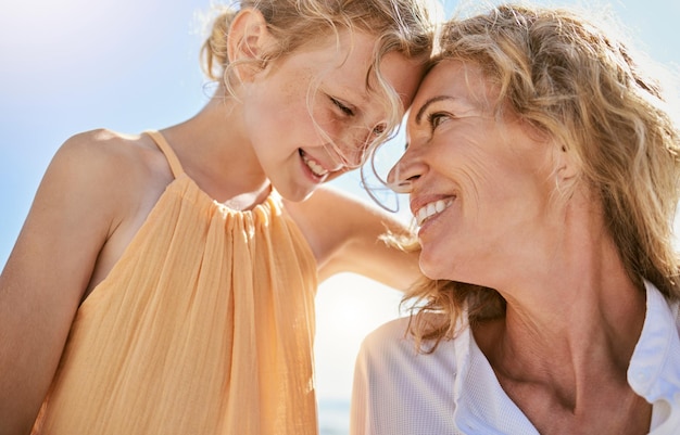 Cheerful mature woman and little girl talking and sharing a secret while sitting on the beach Happy little girl smiling while sitting with her mom or grandmother and being loving and affectionate