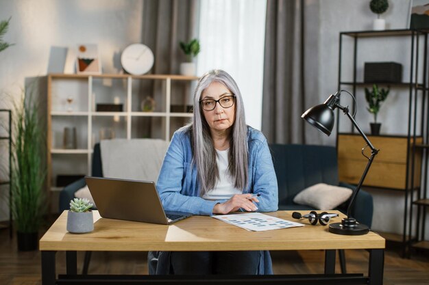 Cheerful mature woman sitting at desk with laptop and looking at camera