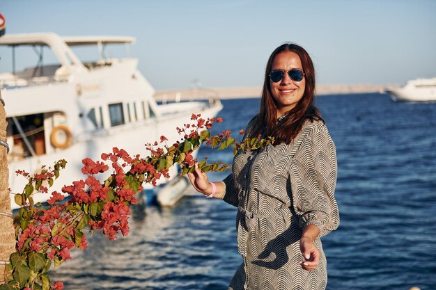 海の上の白いヨットに対して立っている陽気な成熟した女性