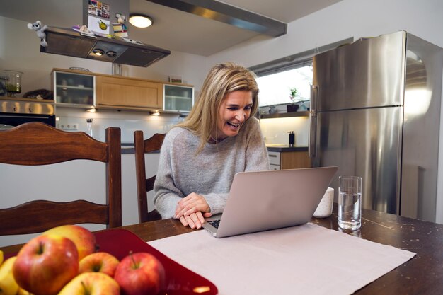 Cheerful mature woman using laptop at home