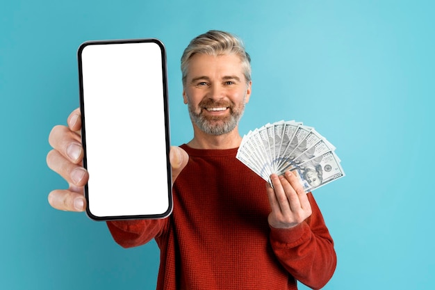 Веселый мужчина средних лет показывает смартфон и деньги
