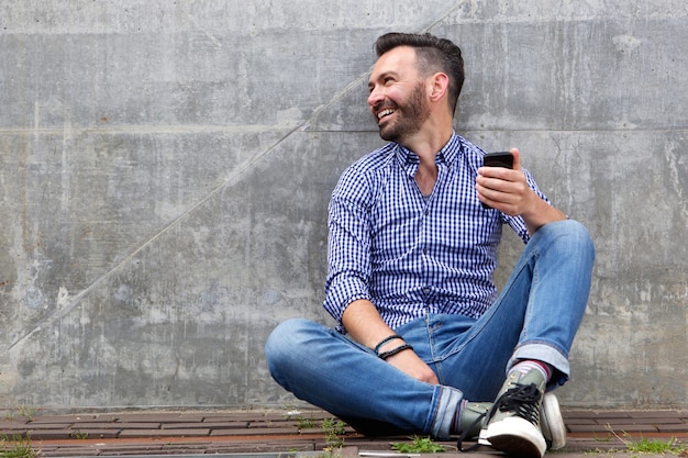 Cheerful middle aged man sitting outside with mobile phone